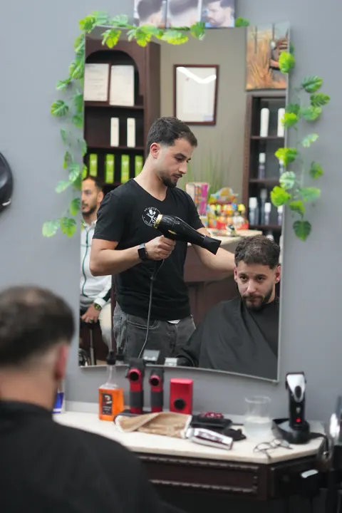 Blick in den Salon: Ein Friseur arbeitet am Spiegelplatz an einem Kunden.