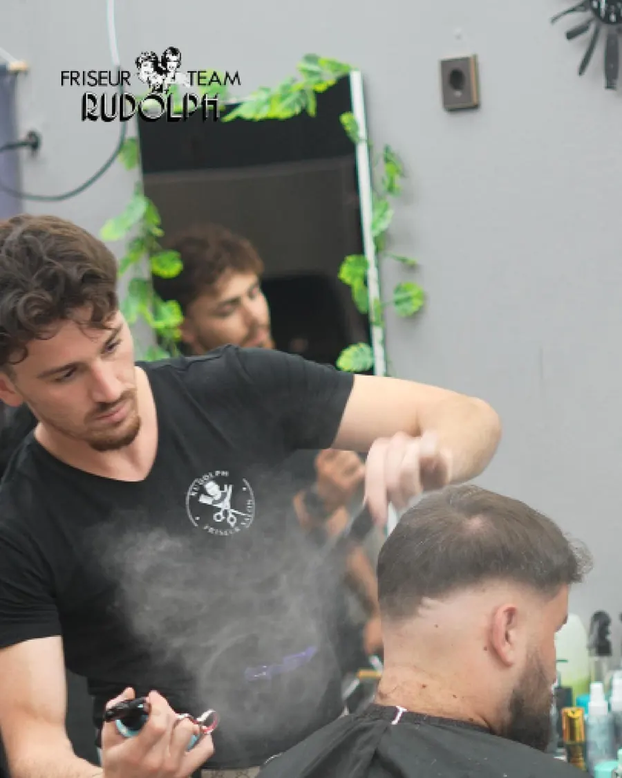 Friseur des Teams Rudolph besprüht beim Schneiden die Haare eines Kunden mit Wasser.